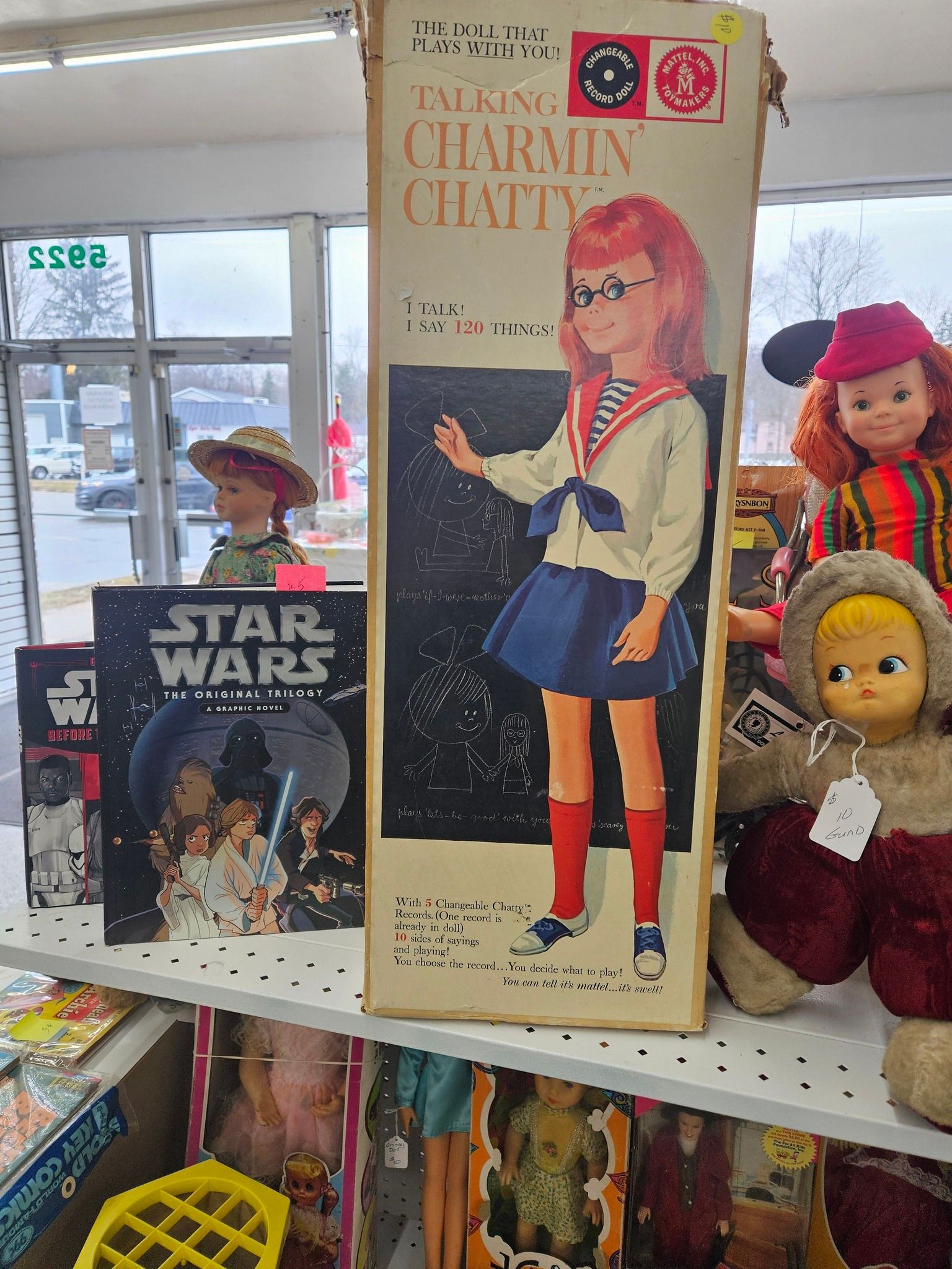 Vintage dolls and toys displayed on a shelf, including a tall doll box and a Star Wars item.