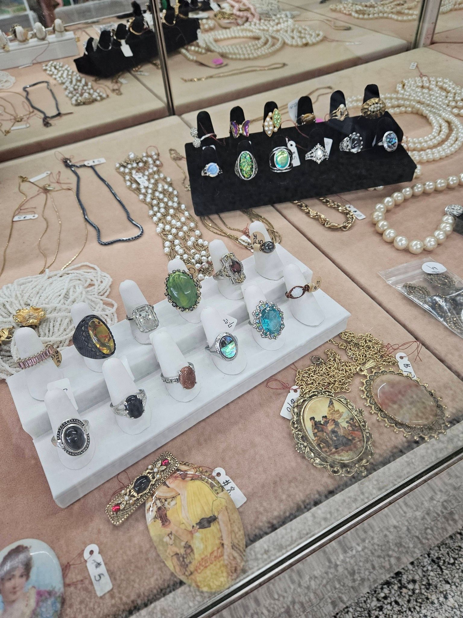 Assorted rings, bracelets, and necklaces displayed on white and black trays at a jewelry stall