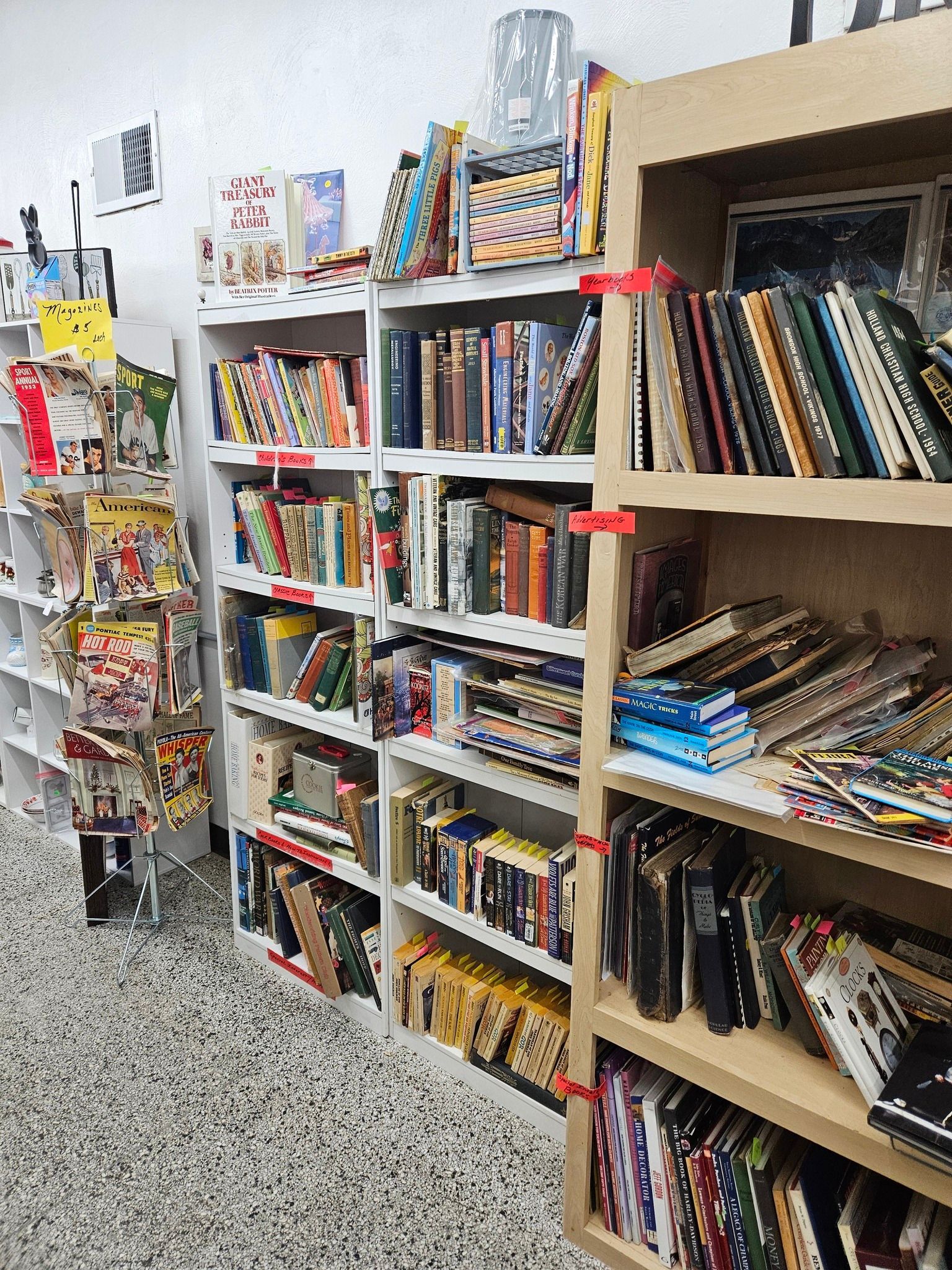 A bookstore aisle with shelves packed with books and magazines, including colorful covers and stacked paperbacks.