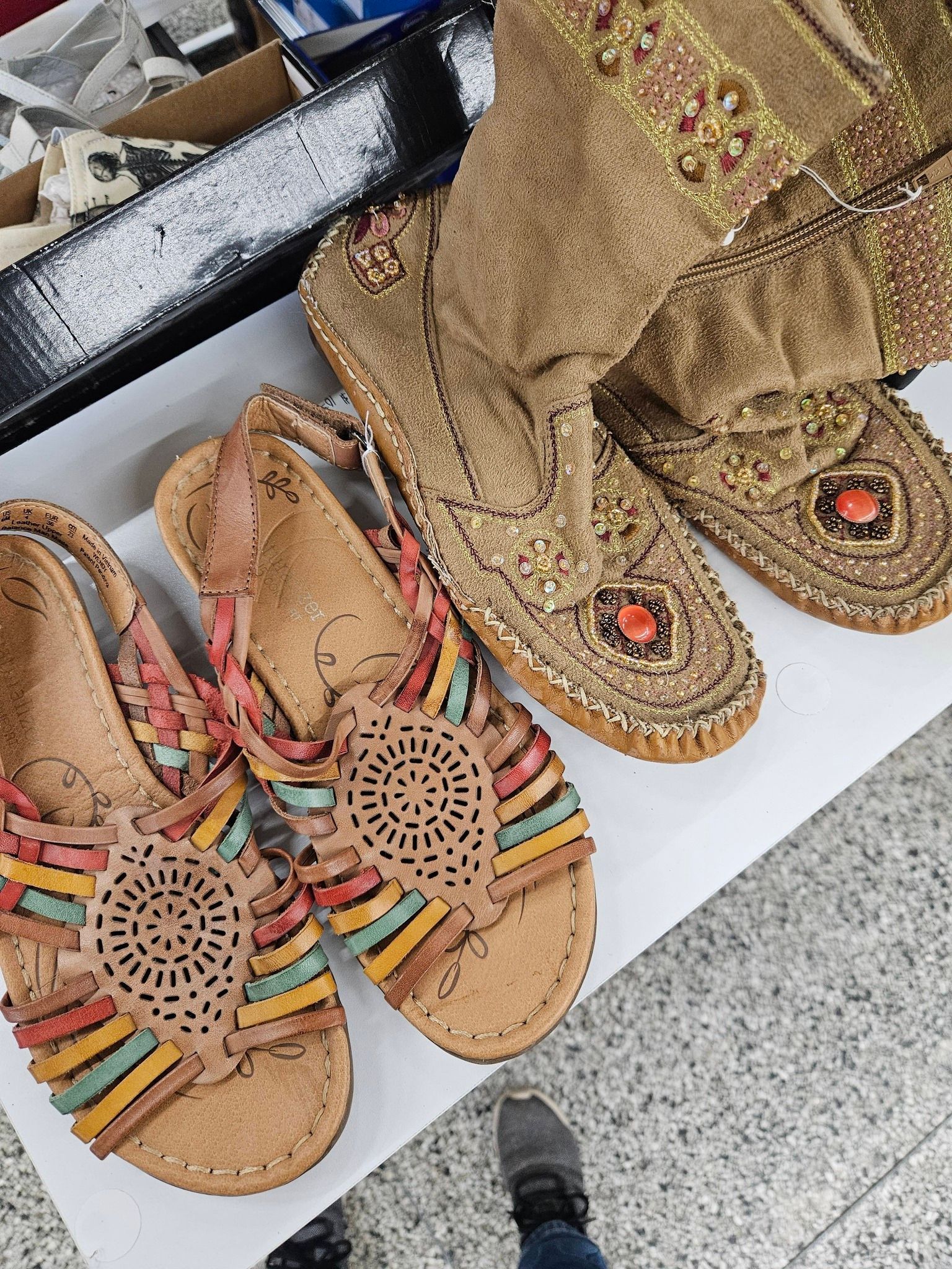 Two pairs of decorative sandals and gold embroidered pants displayed on a floor.