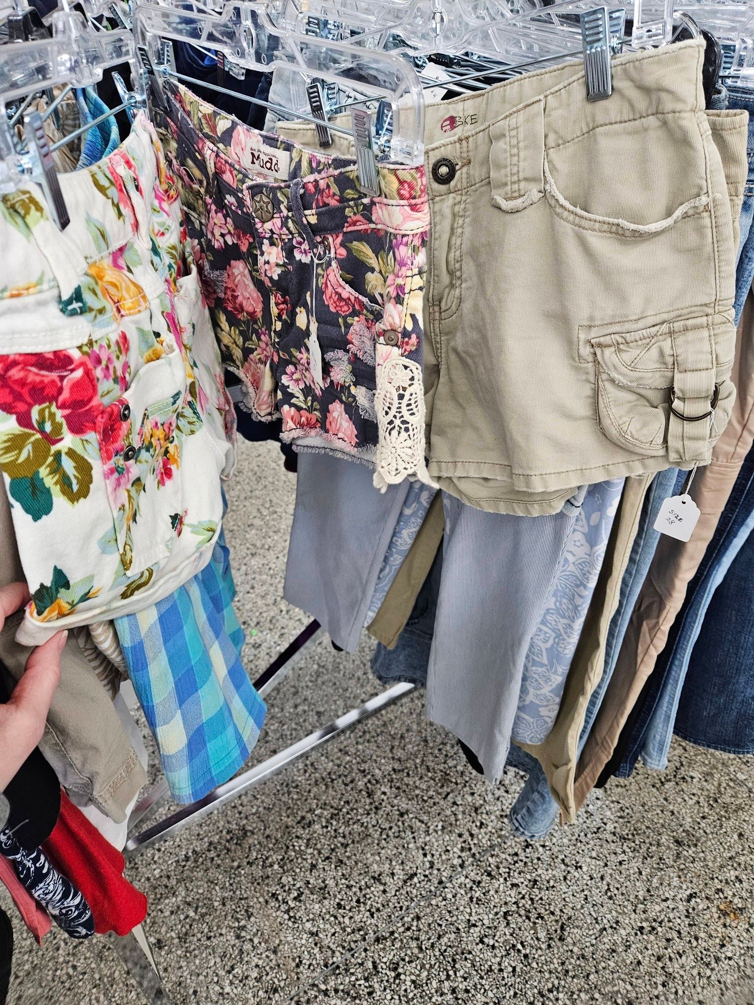 Clothes rack with floral, beige, and striped garments hanging on hangers at an outdoor market.