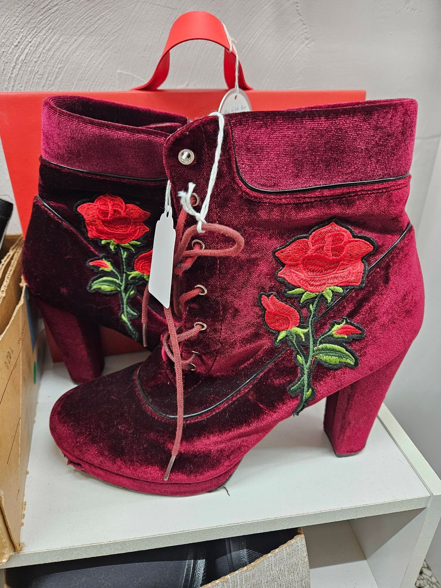 Pink glittery high-heeled handbag with rose embroidery and a red handle on a white table.