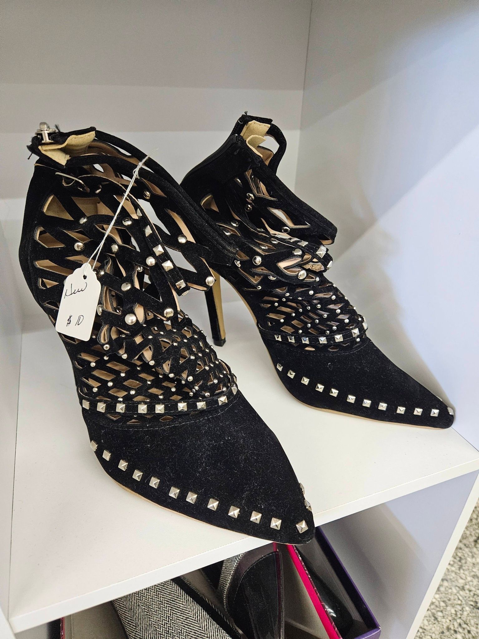 Black studded lace-up ankle boots with high heels on a white shelf display.