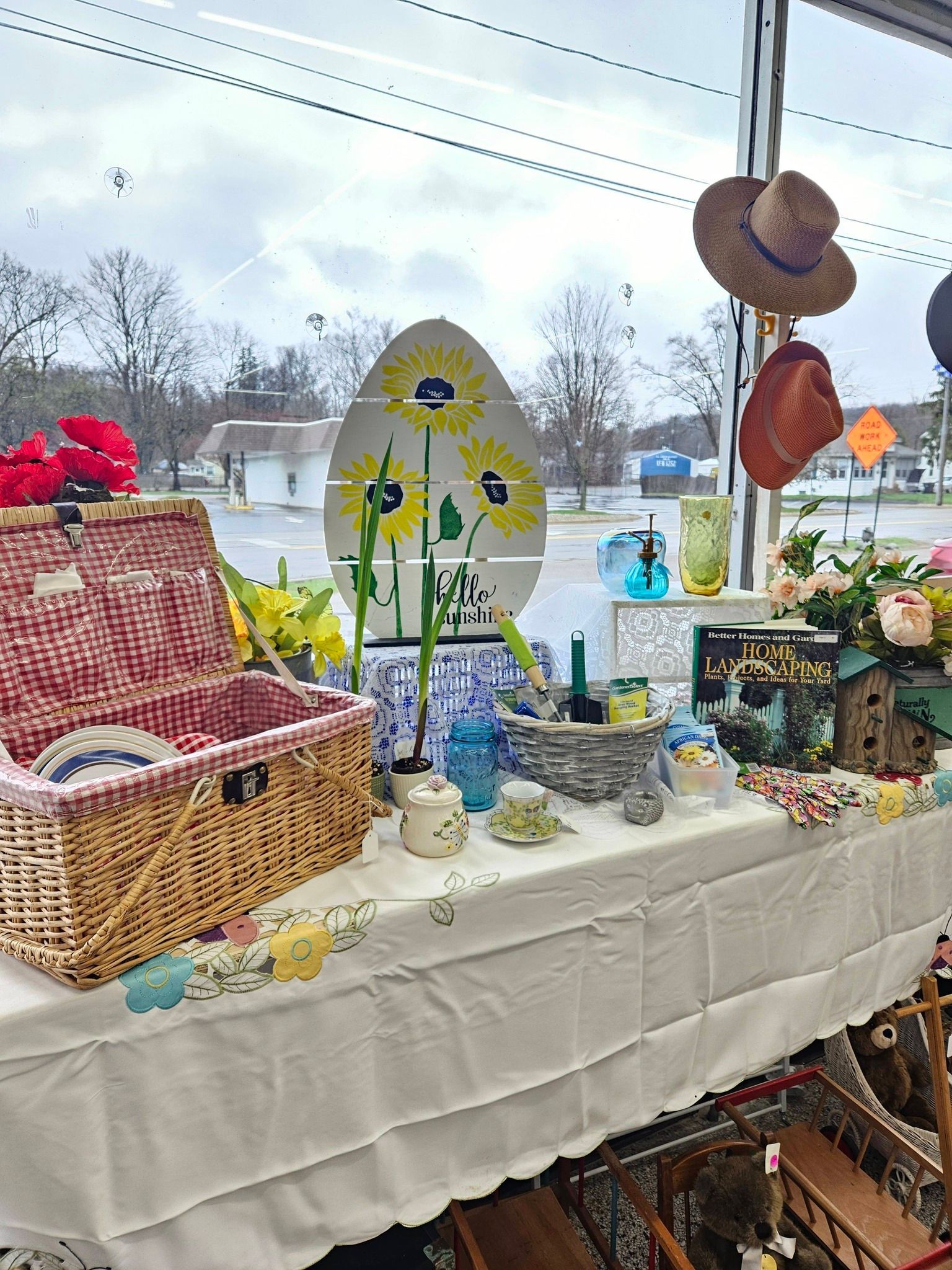 Decorated market table with baskets, flowers, pottery, and hats near a window overlooking a winter scene