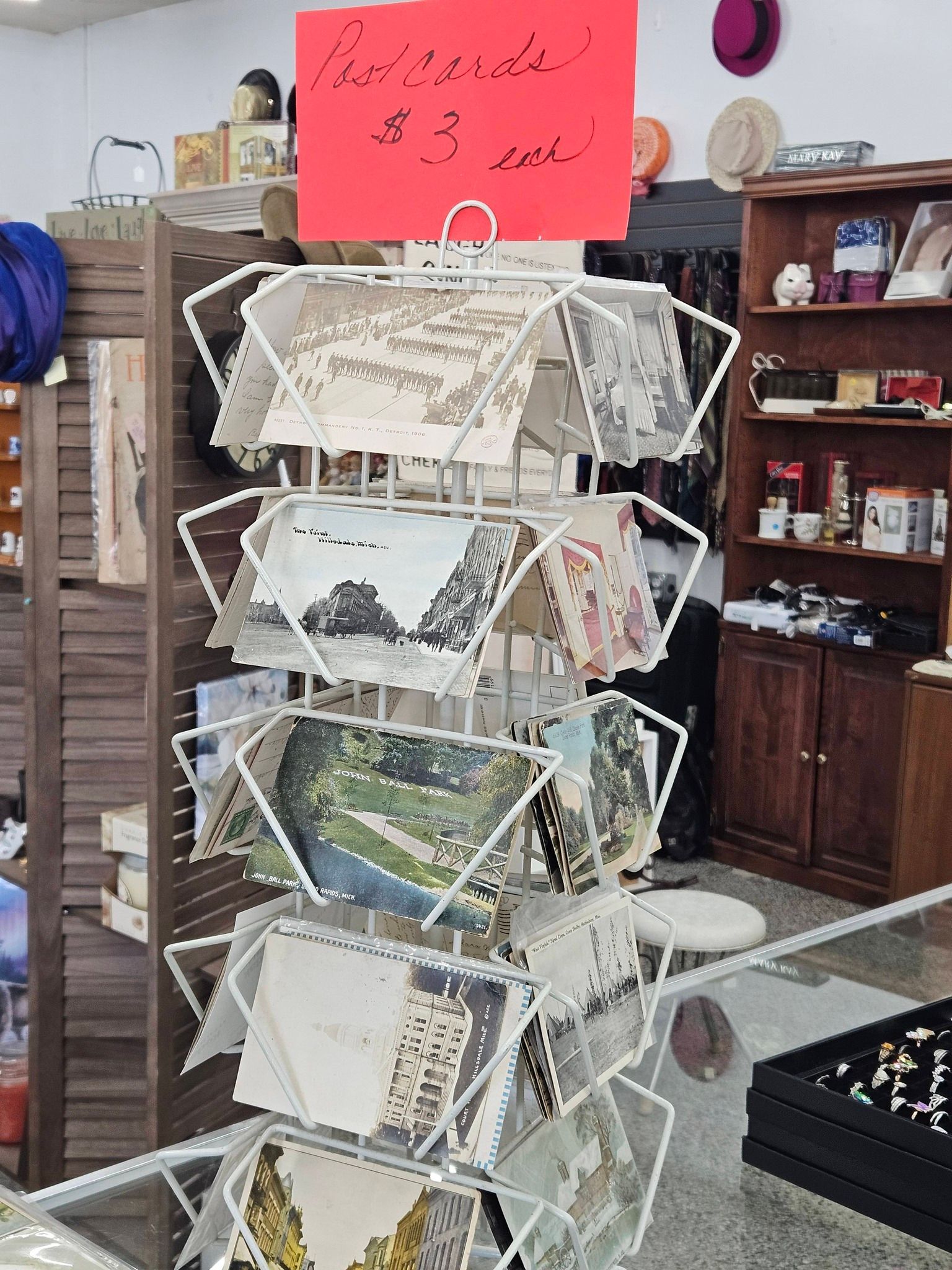 Wire postcard rack in a shop, with postcards and a bright pink sign above it.