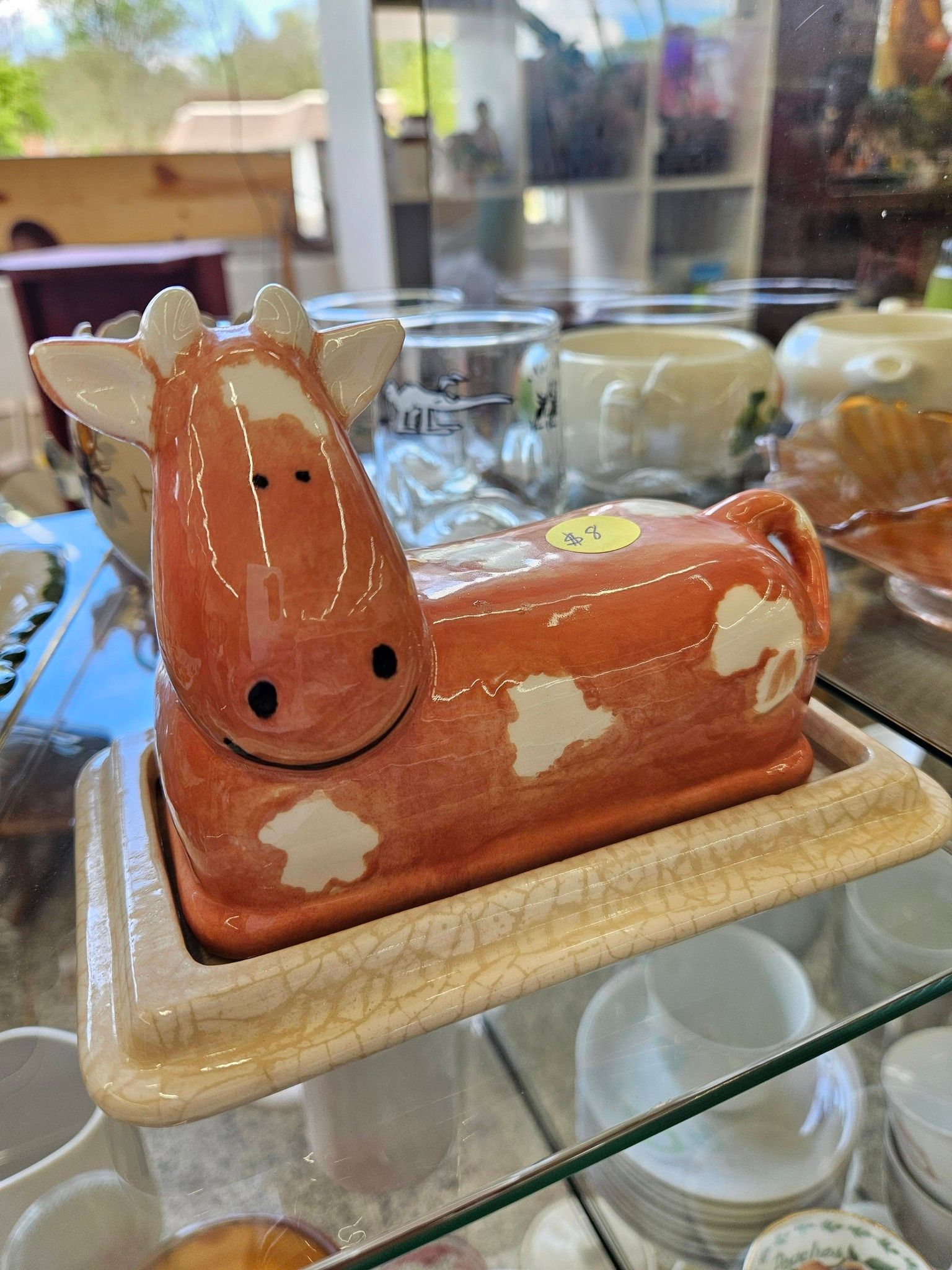 Glossy brown ceramic dog figurine with white spots on a glass shelf