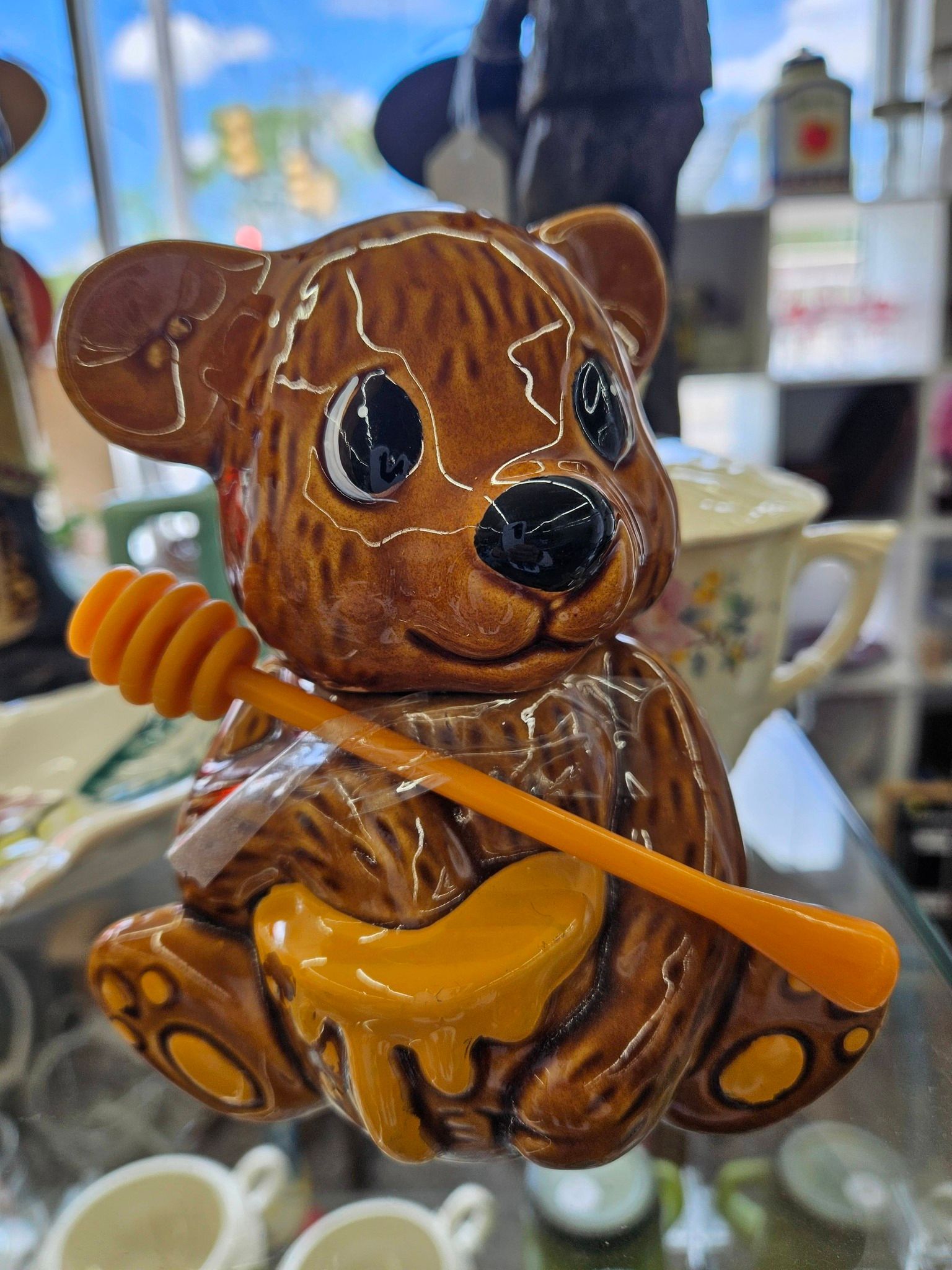 Brown teddy bear figurine holding a honey dipper and pot, with glossy black eyes