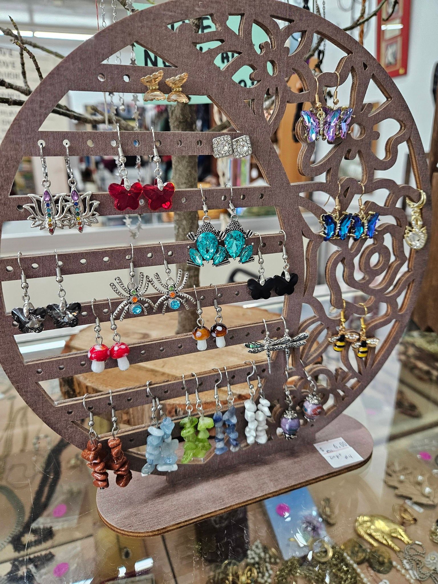 Circular wooden earring display with colorful dangling earrings on shelves in a shop window