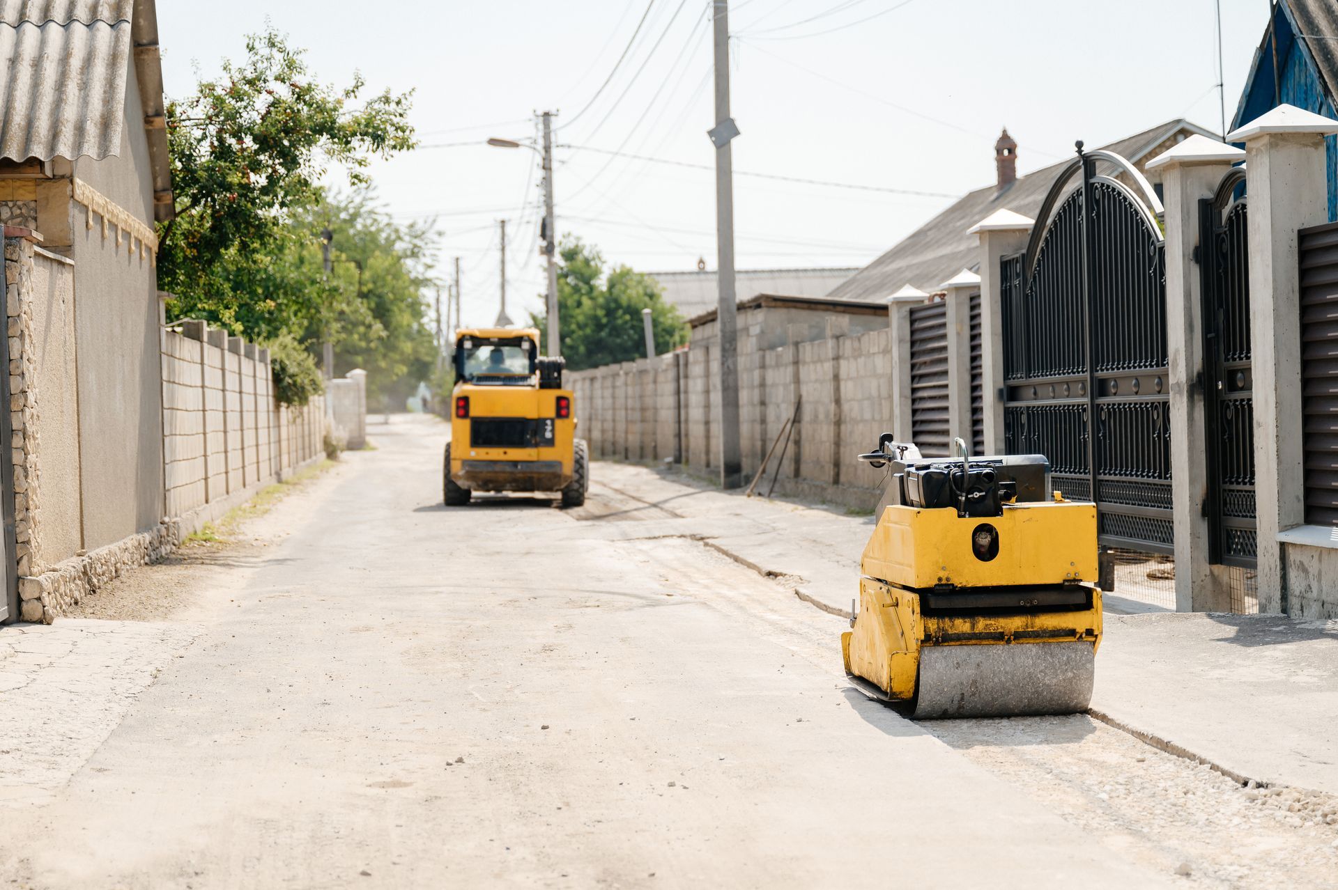Two yellow road rollers on a dusty residential street with walls and utility poles Two yellow road rollers on a dusty residential street with walls and utility poles