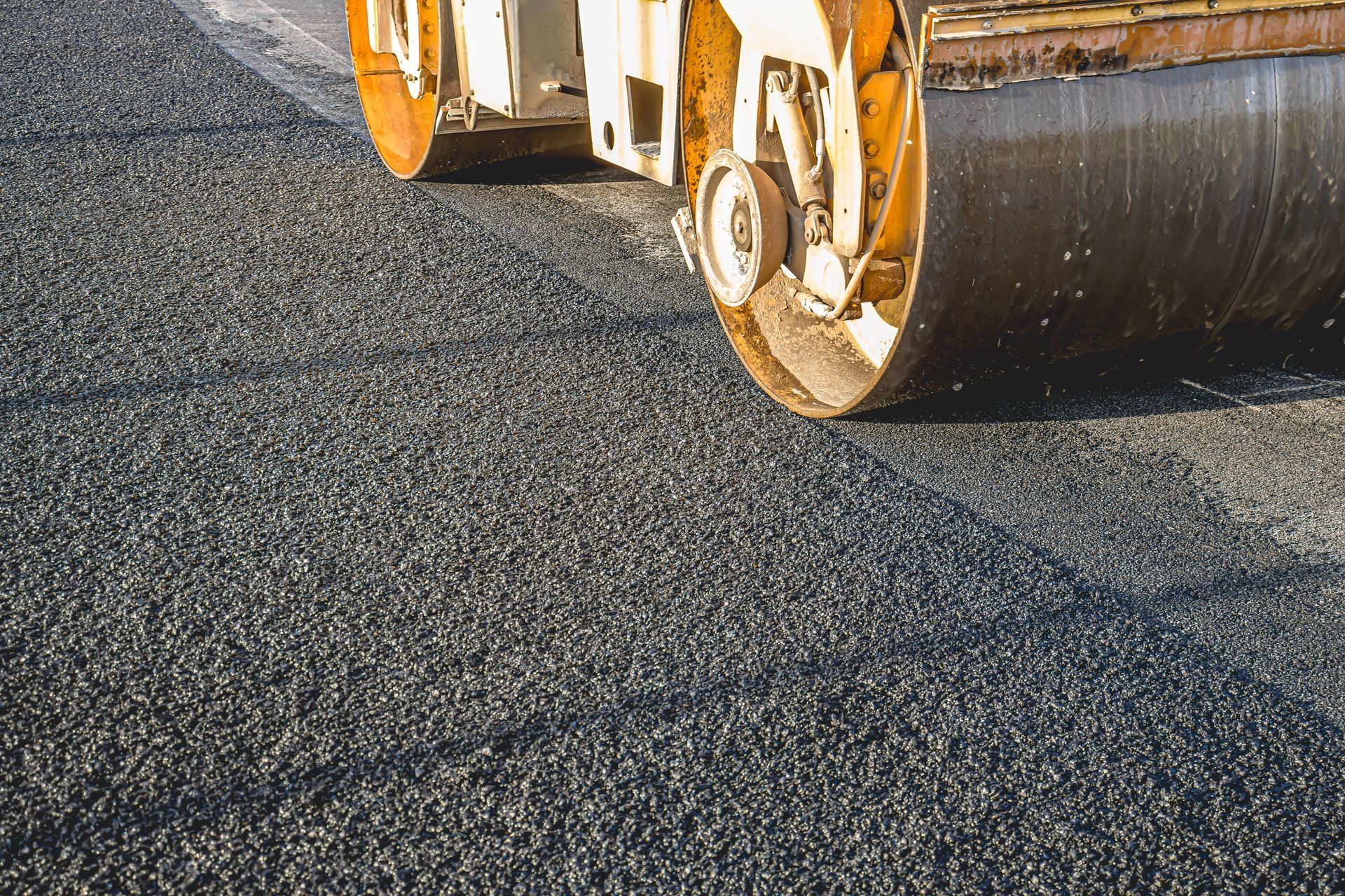 Yellow road roller smoothing wet pavement, with steam rising from the freshly paved surface. Road roller compacting fresh asphalt on a road surface