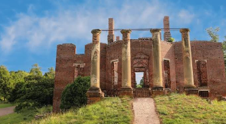 Overgrown brick ruin with tall stone columns and a path leading to the entrance under a blue sky Overgrown brick ruin with tall stone columns and a path leading to the entrance under a blue sky