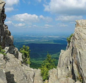 Rocky cliffs framing a distant blue-green valley under a partly cloudy sky Rocky cliffs framing a distant blue-green valley under a partly cloudy sky