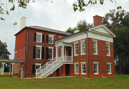 Red-brick historic house with white columns and exterior staircase on a grassy lawn