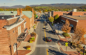 Downtown street with parked cars, brick buildings, autumn trees, and mountains in the background