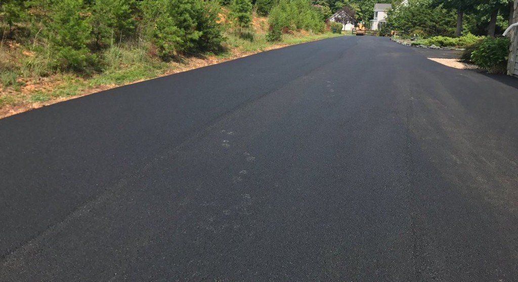 Freshly paved dark asphalt road curving through a green wooded area Freshly paved dark asphalt road curving through a green wooded area