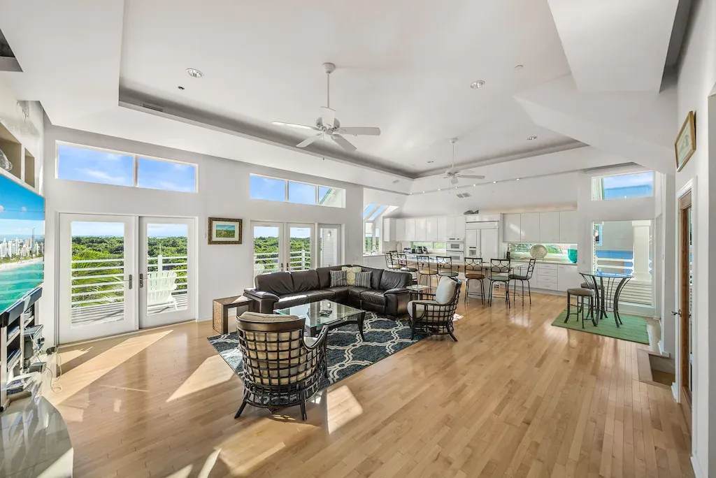 Bright, open living space with wood floors, large windows, and a sectional sofa with ocean view.