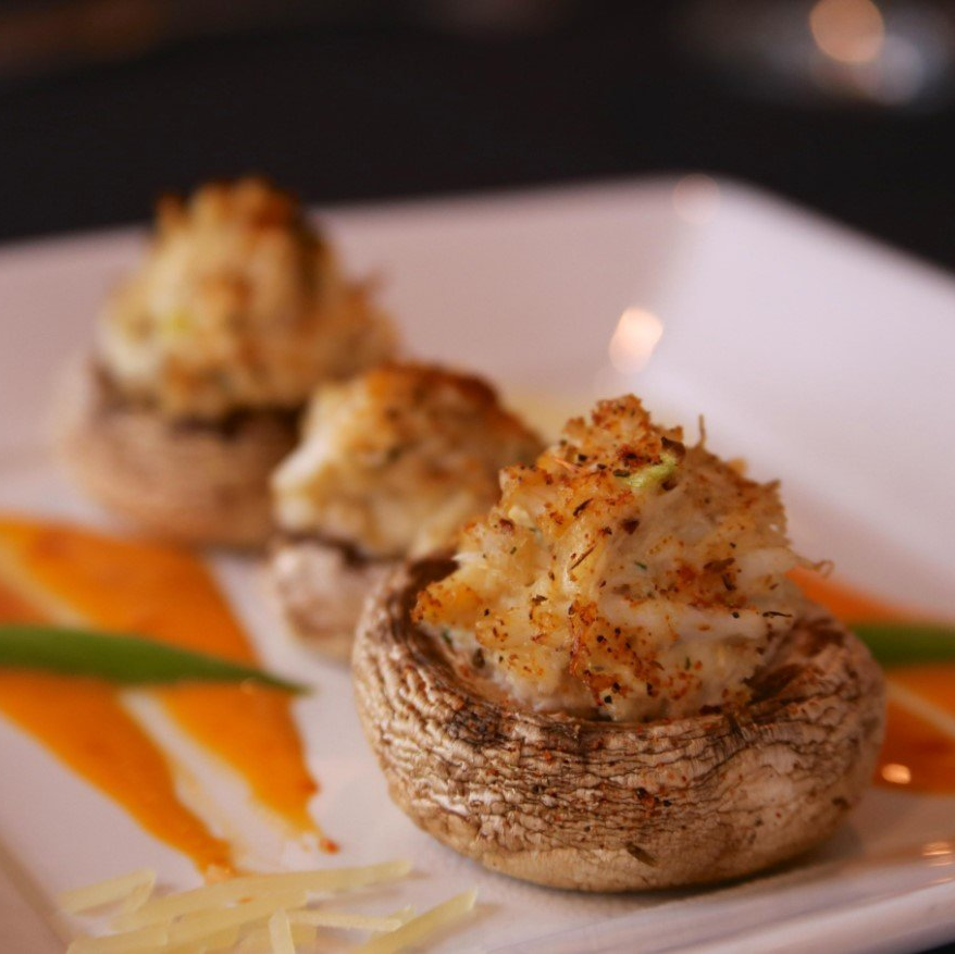 Stuffed mushrooms on a white plate with orange sauce, a garnish, and a dark background.