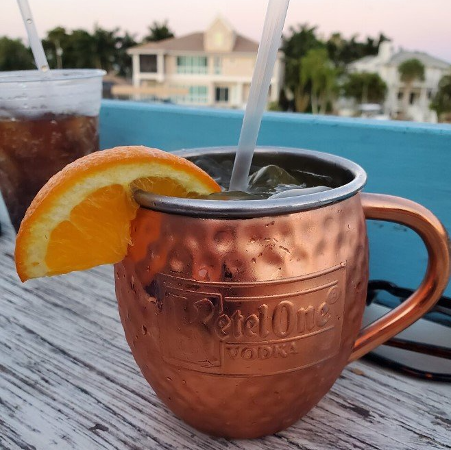 Copper mug with an orange slice and a drink, on a deck with a view of houses.