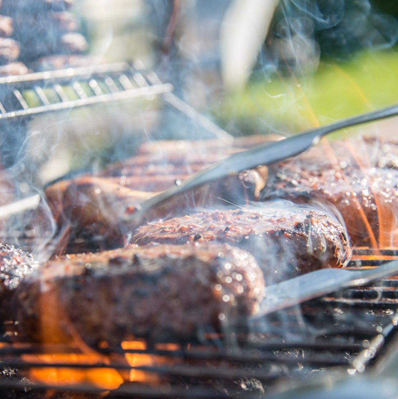 Burgers grilling on a barbecue, smoke rising, tongs flipping.