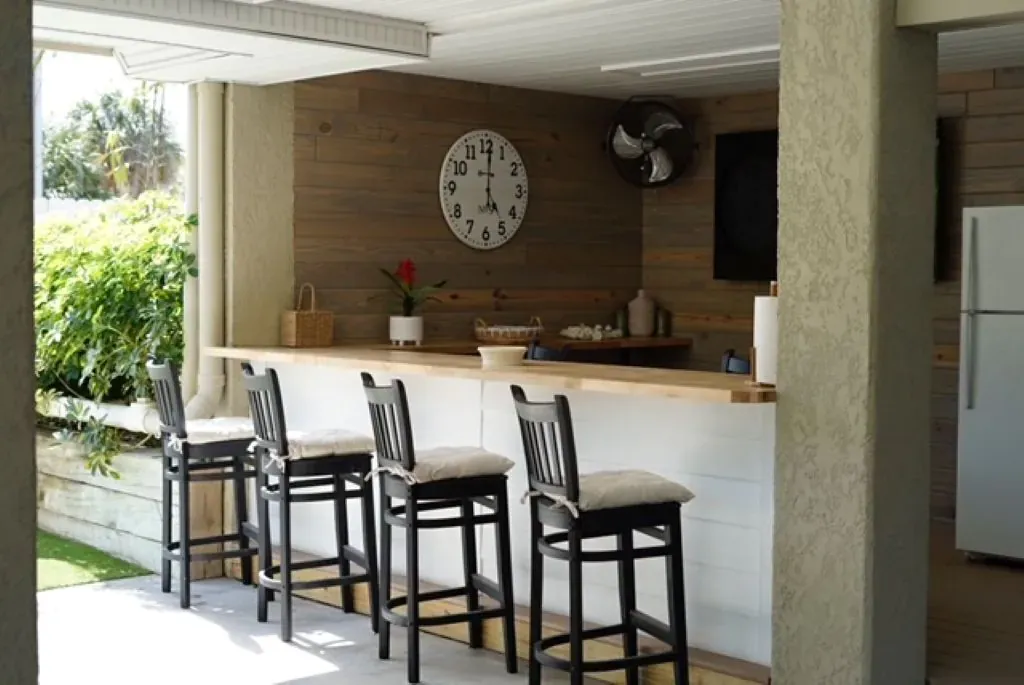 Outdoor bar with stools, wood paneling, clock, and a refrigerator.