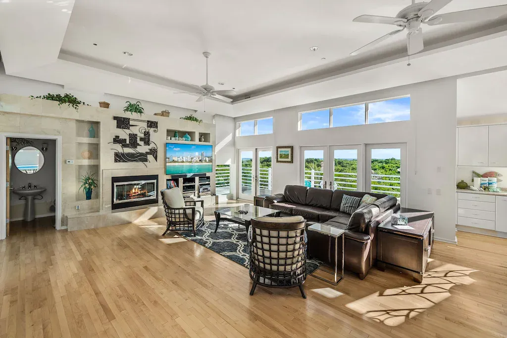 Bright living room with hardwood floors, large windows, fireplace, and leather sectional.