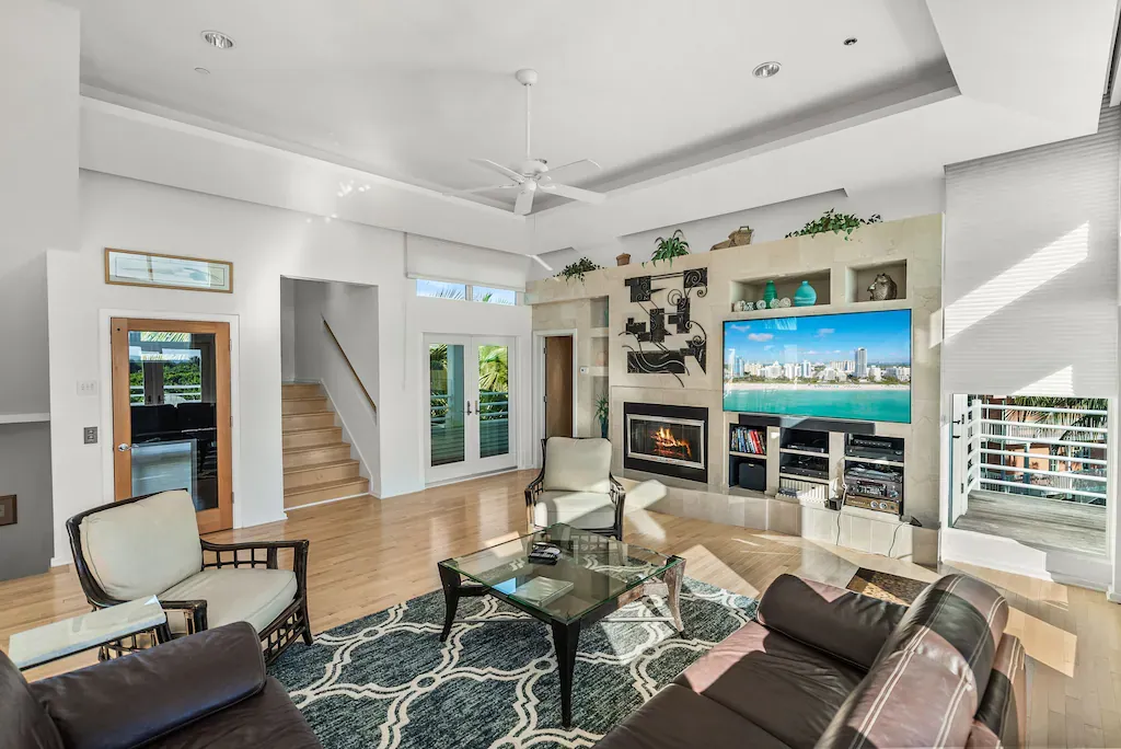 Spacious living room with leather sofa, fireplace, and large TV displaying a beach scene.