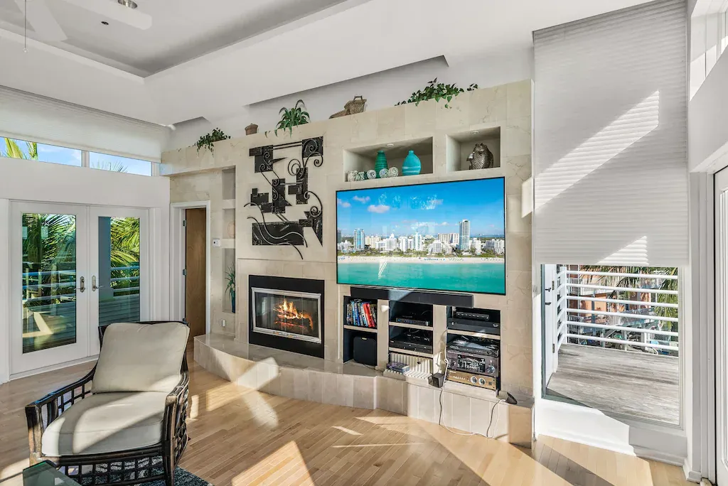 Living room with fireplace, built-in TV, and open doors to a patio with a chair.