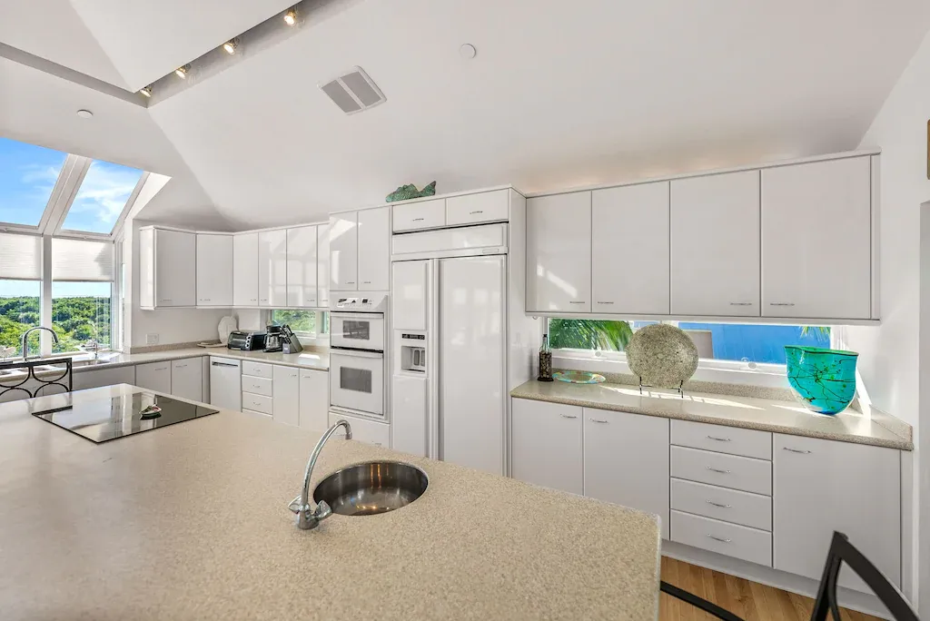 Modern white kitchen with skylights, island, and stainless steel appliances.