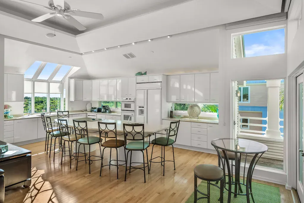 Bright white kitchen with an island, chairs, and windows.