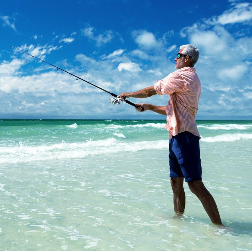 Man fishing in shallow turquoise water under a bright blue sky.