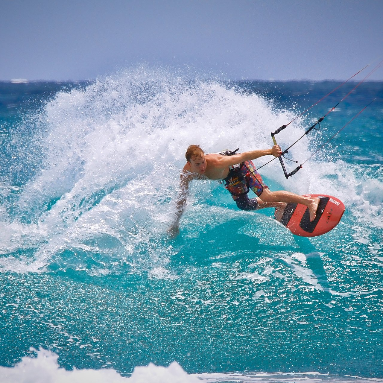 Man kitesurfing on a wave, turquoise water, clear sky.