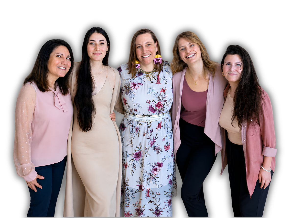 Five women standing together, smiling in casual and floral outfits against a white background