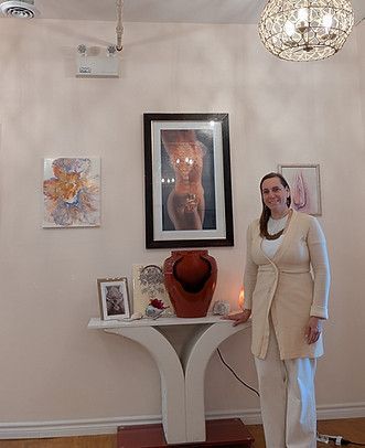 Woman standing beside a white console table in an art-filled room with framed paintings and a chandelier