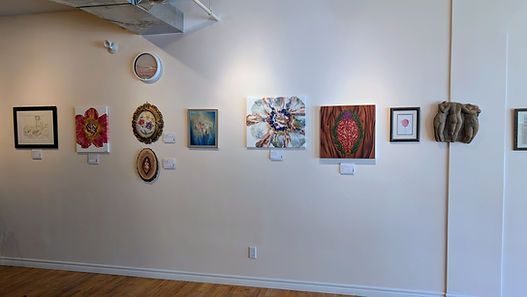 Art gallery wall with a row of colorful framed paintings and small sculptures in a bright room.