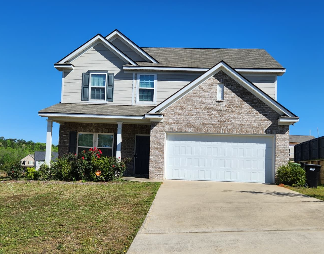 Two-story house with gray horizontal siding, a tan brick front, a white garage door, and a concrete driveway.