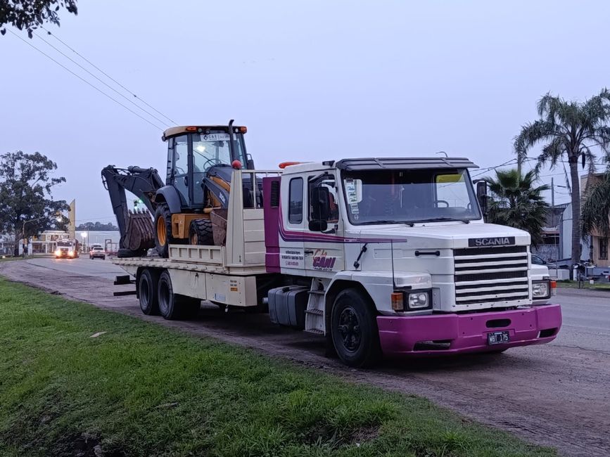 Grúa blanca con retroexcavadora en la cuneta al anochecer.