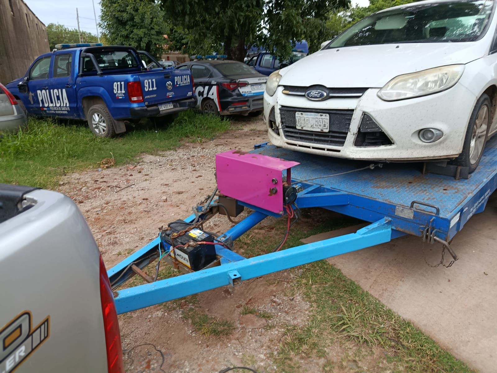 Una furgoneta policial azul y un coche plateado se detuvieron al borde de un camino de tierra, con agentes y gente cerca.