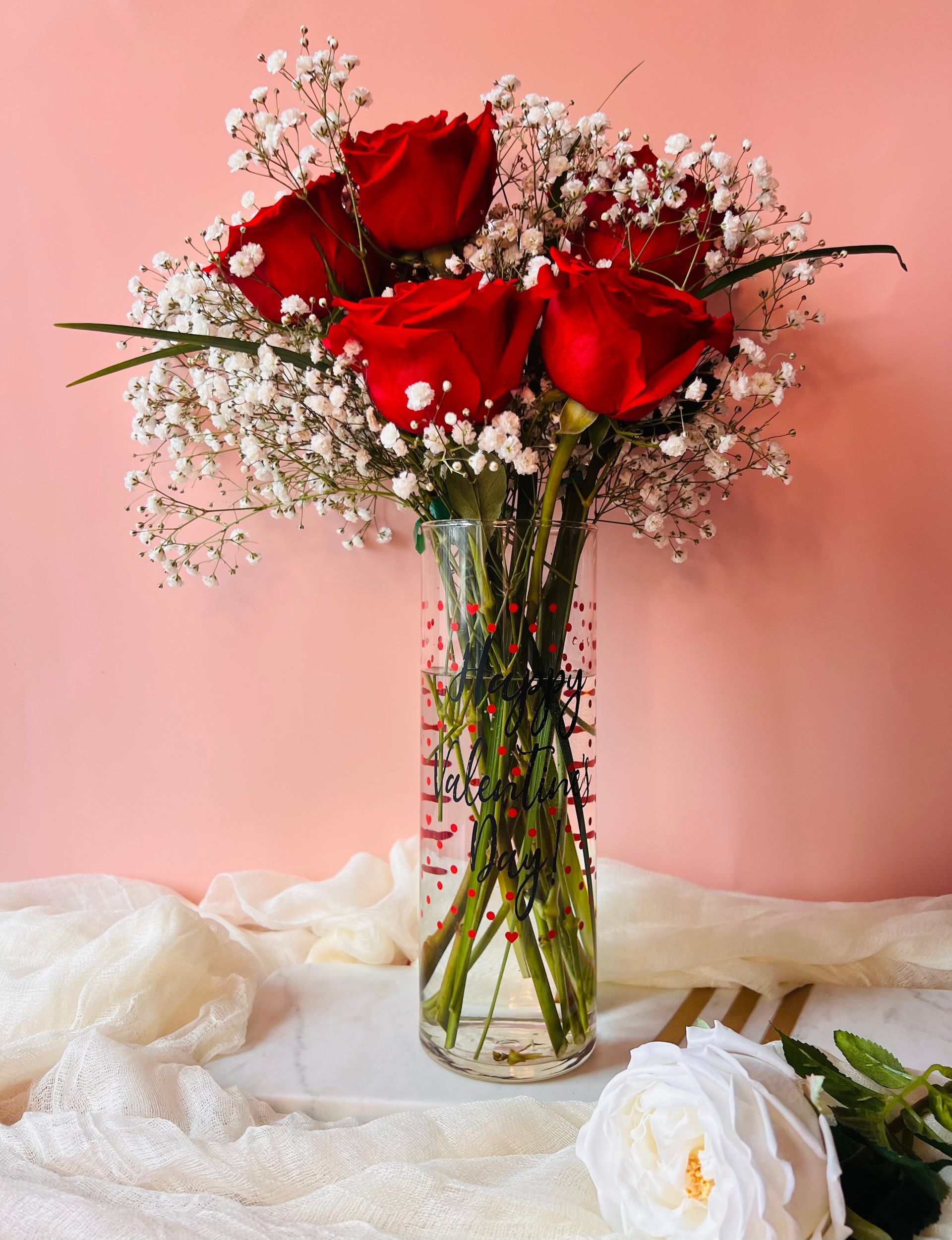 A vase filled with red roses and baby 's breath on a table.