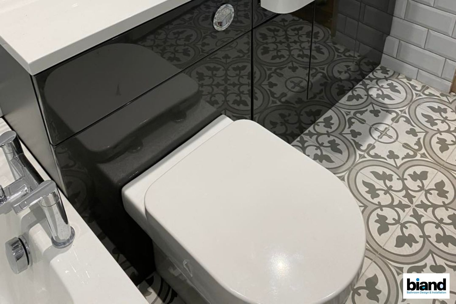 Bathroom with white toilet, gray vanity, patterned floor tiles, and white subway tile wall.