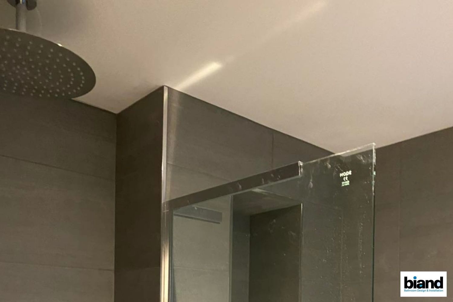 Shower interior with a rain showerhead, gray tile walls, and glass shower partition.