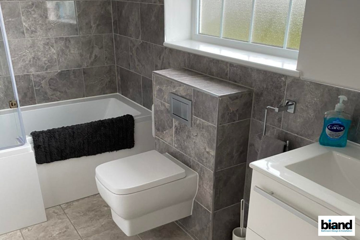 Modern bathroom with gray marble tiles, a white toilet, tub, and vanity.