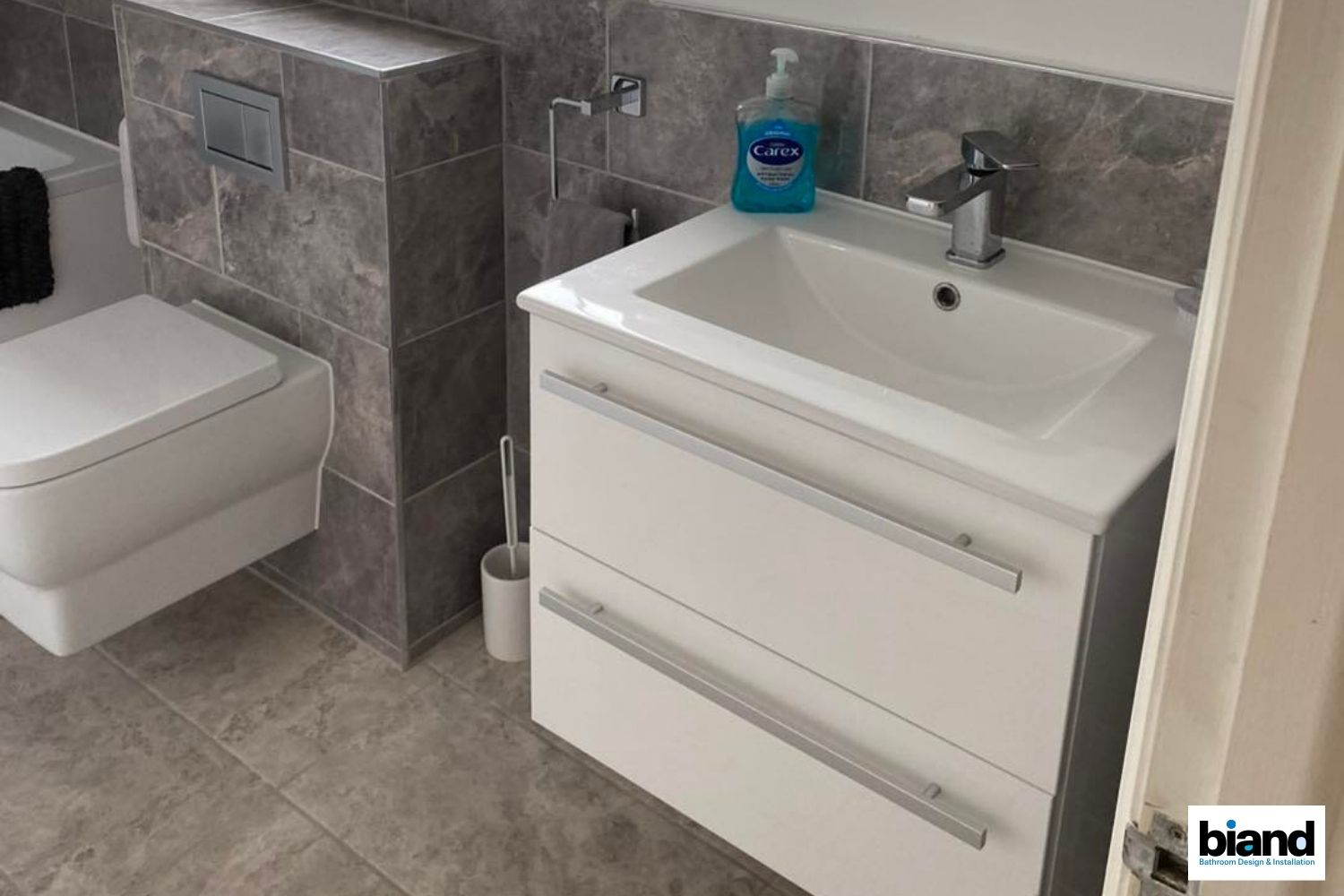 Modern bathroom with white vanity, toilet, and grey tiled walls.