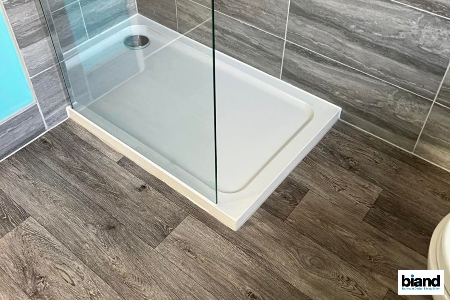 Shower stall with gray floor, white base, glass door, and gray tile wall.