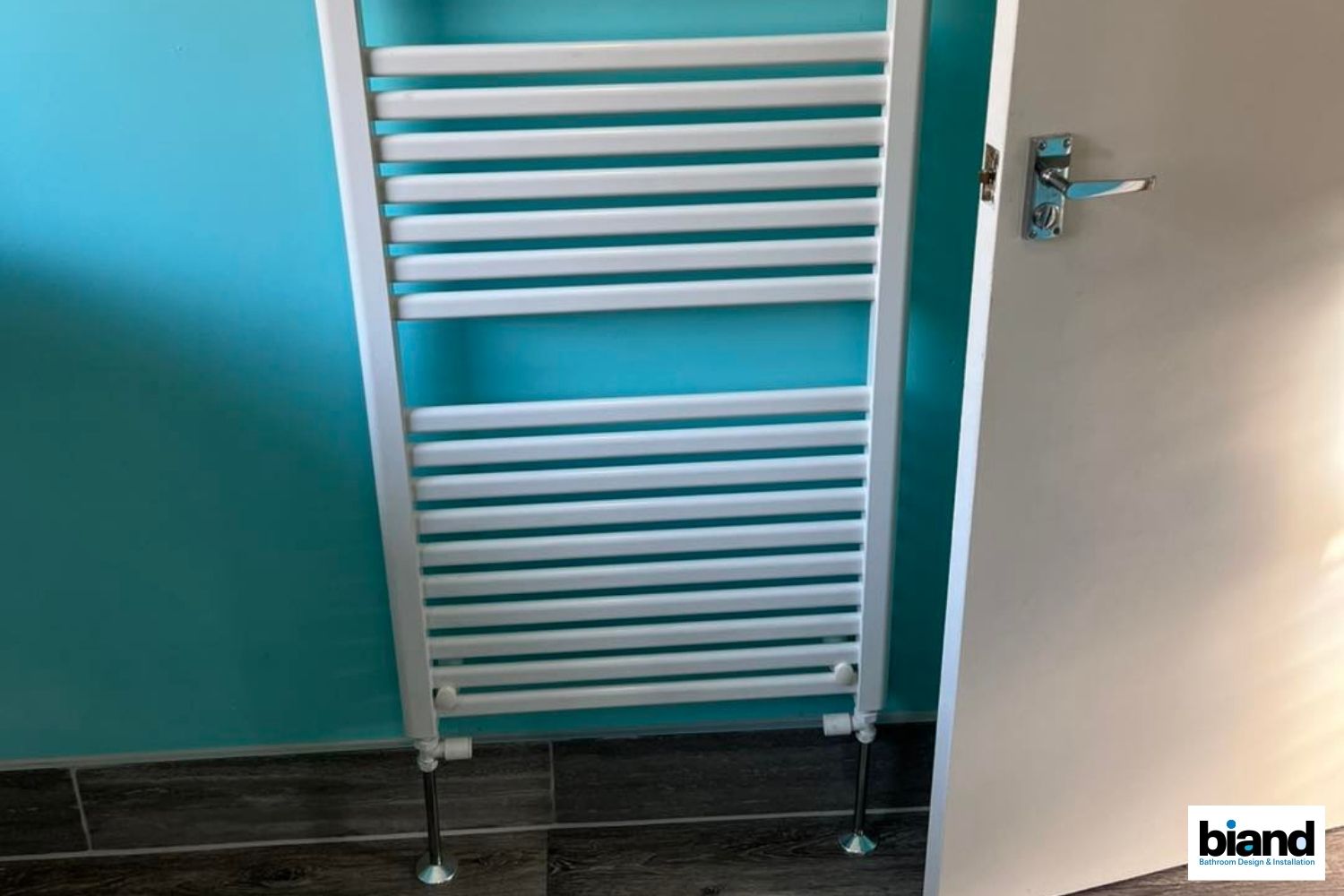 White towel radiator on a turquoise wall. Door is open to the right.