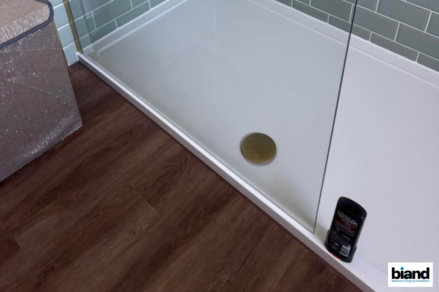 White shower base with a drain, glass panel, and a phone, set on dark wooden flooring.