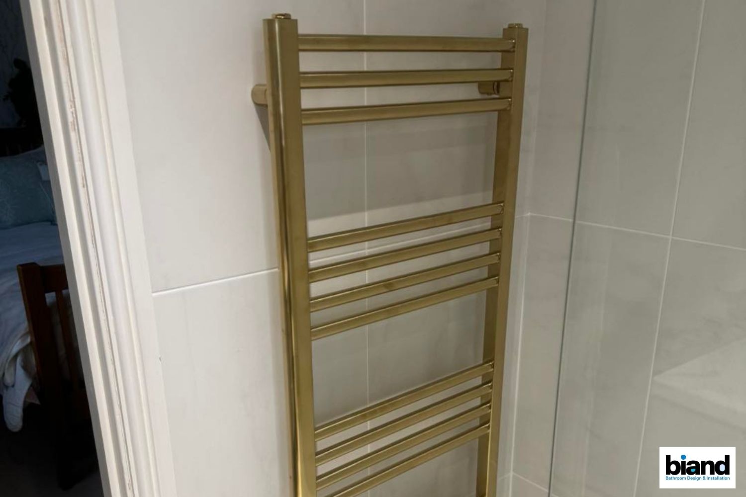 Gold towel rack mounted on a white tiled bathroom wall.
