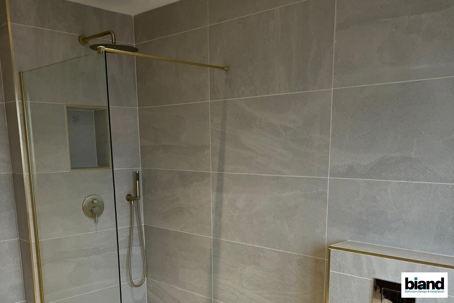 Shower with gold fixtures and gray tiled walls.