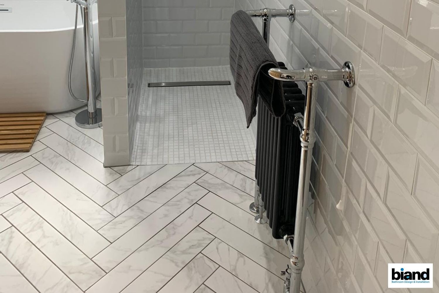 Herringbone tile bathroom with black towel rack.