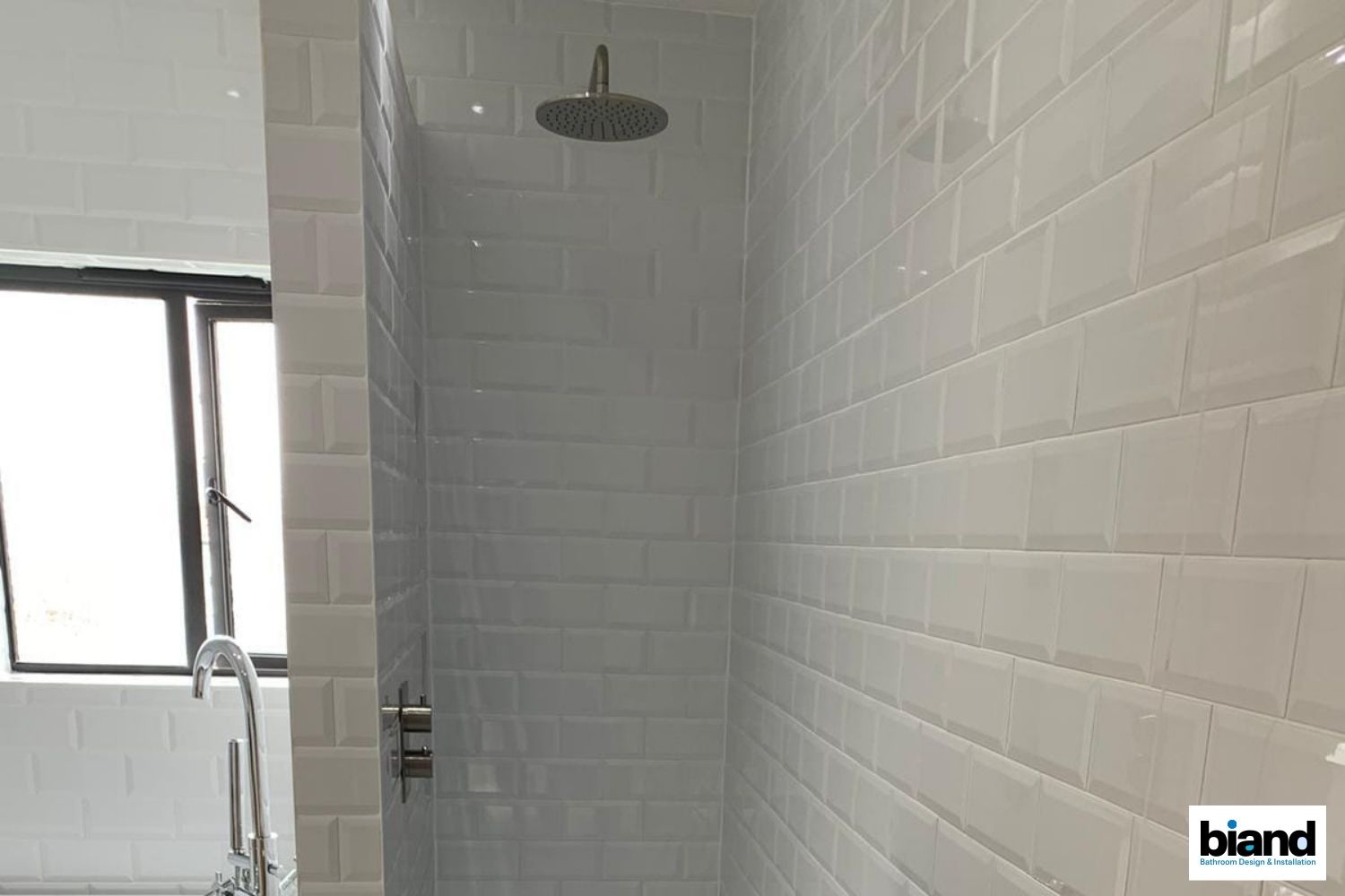 White tiled shower with rain showerhead and fixtures.