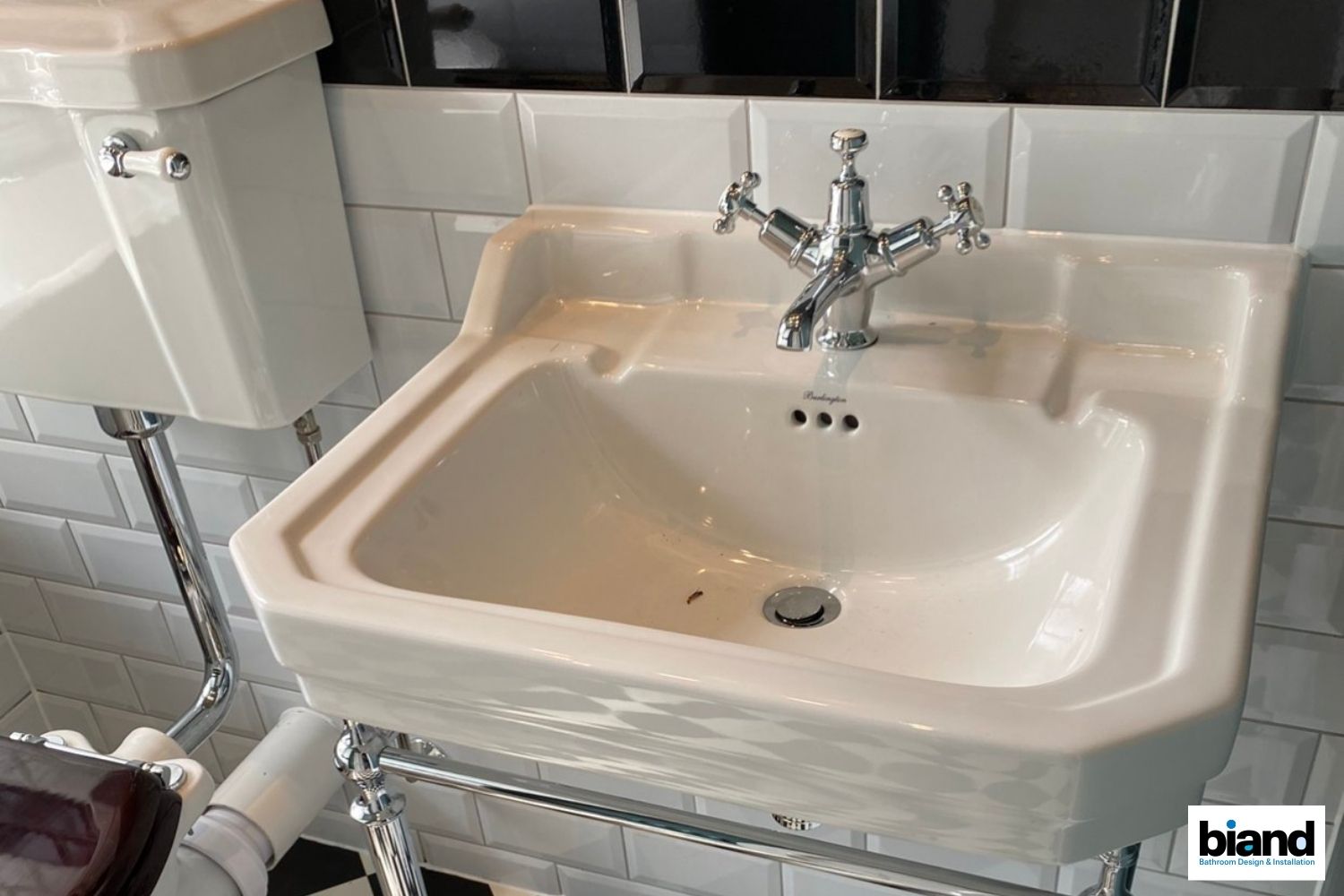 Cream-colored porcelain sink with chrome faucet and drain, on a white tiled wall.